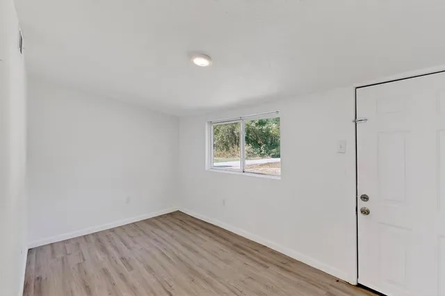 a view of an empty room with wooden floor and a window