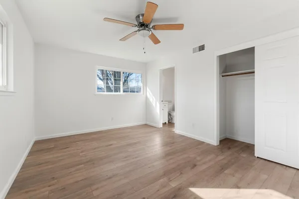 an empty room with wooden floor ceiling fan and windows