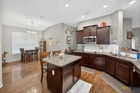 a kitchen with stainless steel appliances granite countertop a kitchen island a stove a sink a refrigerator dining table and chairs