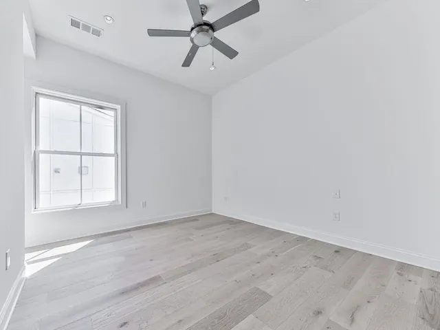 an empty room with wooden floor ceiling fan and windows