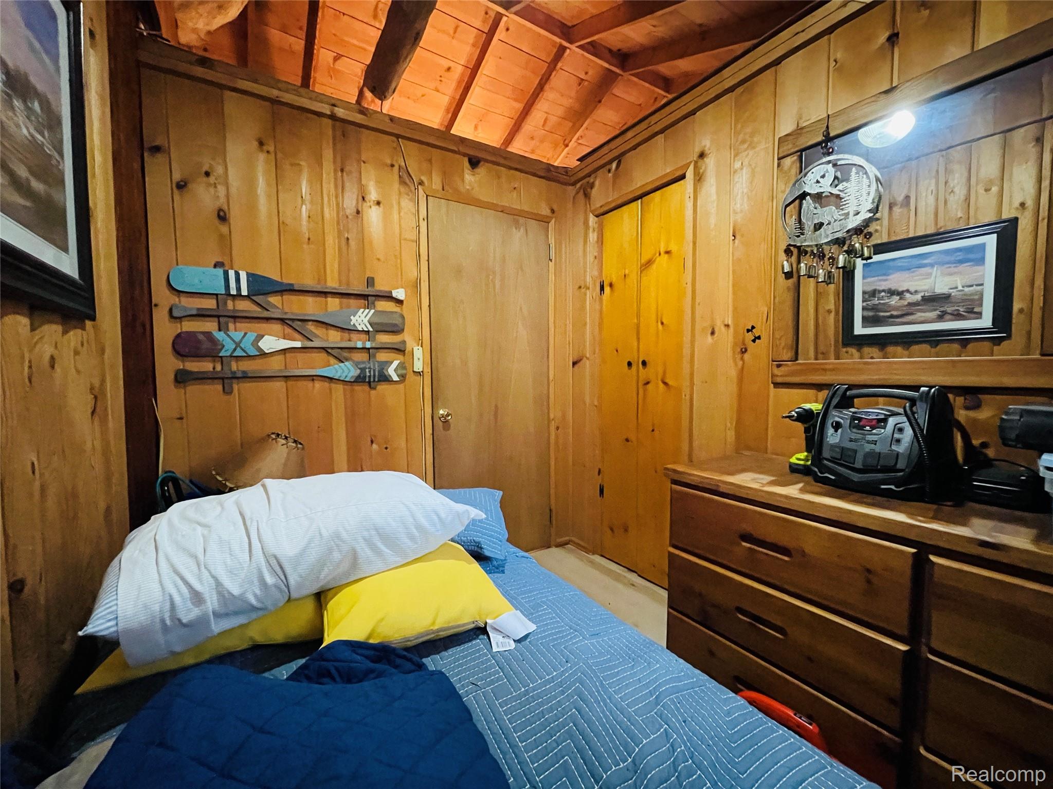 417 Ogemaw Road Rose City, MI 48654 - Photo 11 of 26 Wood-paneled walls with exposed beam ceiling, wood-finish flooring, and a built-in wood dresser