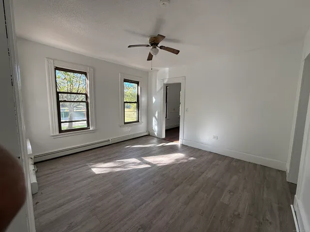 an empty room with wooden floor chandelier fan and windows