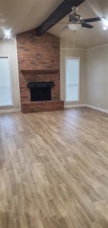 an empty room with wooden floor fireplace and windows