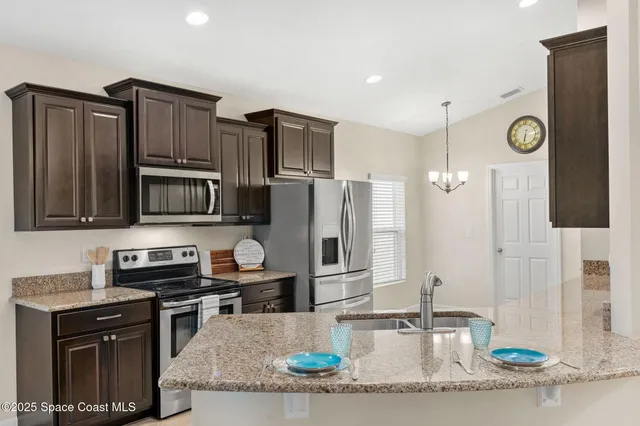 a kitchen with stainless steel appliances granite countertop a refrigerator a stove and a sink with wooden cabinets