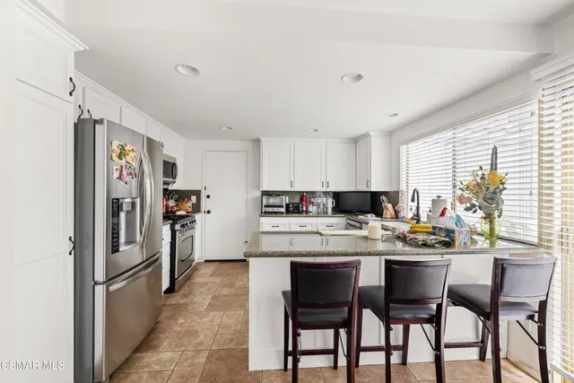 a kitchen with stainless steel appliances kitchen island granite countertop a table chairs refrigerator and window