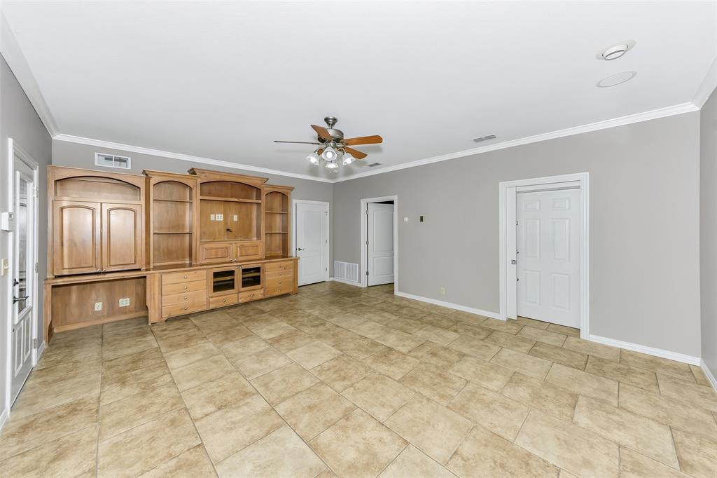566 Selma Park Road Bowie, TX 76230 - Photo 16 of 40 Spacious room featuring tile flooring, light gray walls, a built-in entertainment center with extensive cabinetry and shelving, a ceiling fan with integrated lighting, and crisp white crown molding