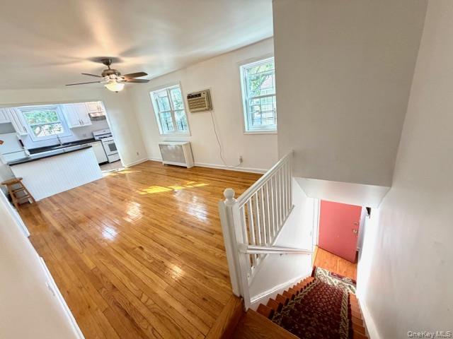 Staircase with wood-type flooring, ceiling fan, radiator, and a wall unit AC