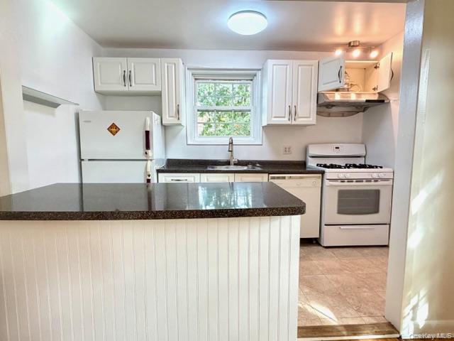 65-26B 223rd Place, Unit 2 Queens, NY 11364 - Photo 3 of 30 EAST window -Kitchen featuring white appliances, white cabinetry, under cabinet range hood, dark stone countertops, and light tile patterned floors