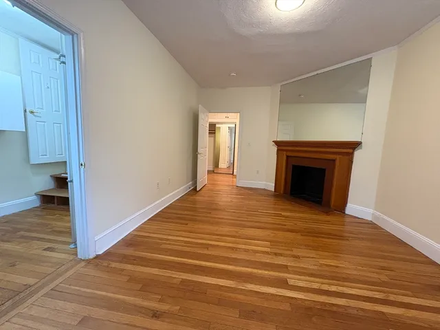 a view of an empty room with wooden floor fireplace and a window