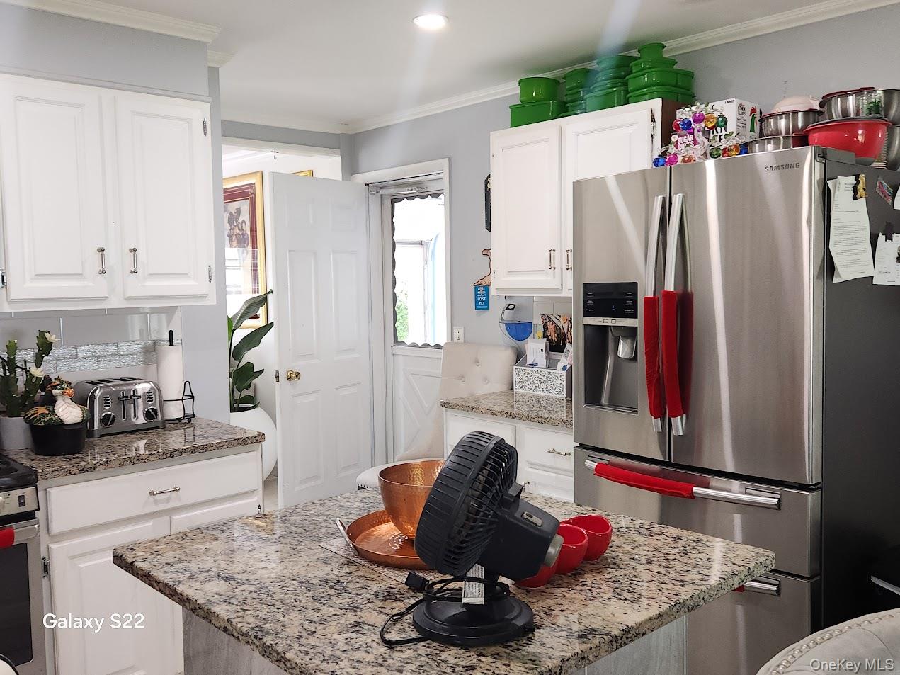 46 Randolph Road White Plains, NY 10607 - Photo 6 of 16 Kitchen with stainless steel fridge with ice dispenser, white cabinetry, ornamental molding, a kitchen island, and light stone counters
