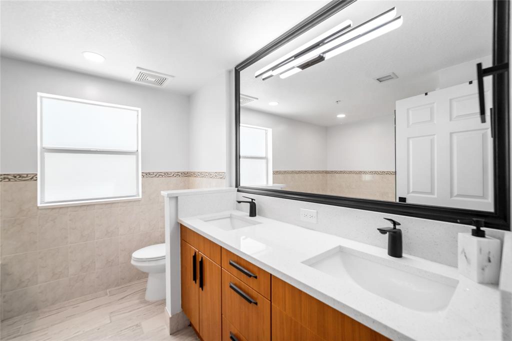 3210 Northeast 5th Street, Unit 203 Pompano Beach, FL 33062 - Photo 32 of 61 a bathroom with a double vanity sink a toilet and a mirror