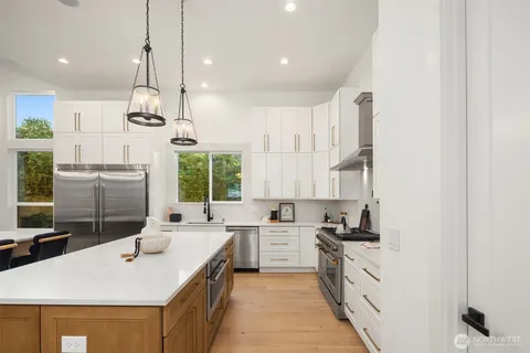 a kitchen with stainless steel appliances kitchen island a sink a stove a refrigerator and white cabinets