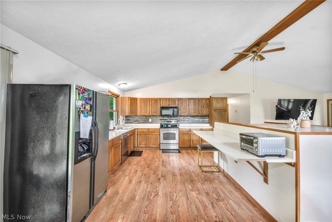 4560 Arrow Road Northwest Carrollton, OH 44615 - Photo 11 of 41 Kitchen featuring light wood-type flooring, vaulted ceiling with beams, appliances with stainless steel finishes, tasteful backsplash, and ceiling fan