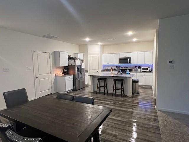 1908 Marquette Road Princeton, TX 75407 - Photo 3 of 14 Open-concept kitchen and dining area featuring white shaker cabinetry, stainless steel appliances, a center island with bar seating, recessed lighting, and wood-finish flooring