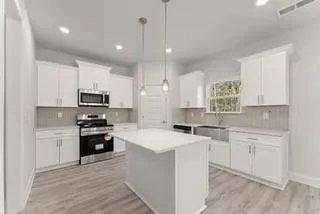 a kitchen with stainless steel appliances kitchen island a sink a stove a refrigerator and white cabinets