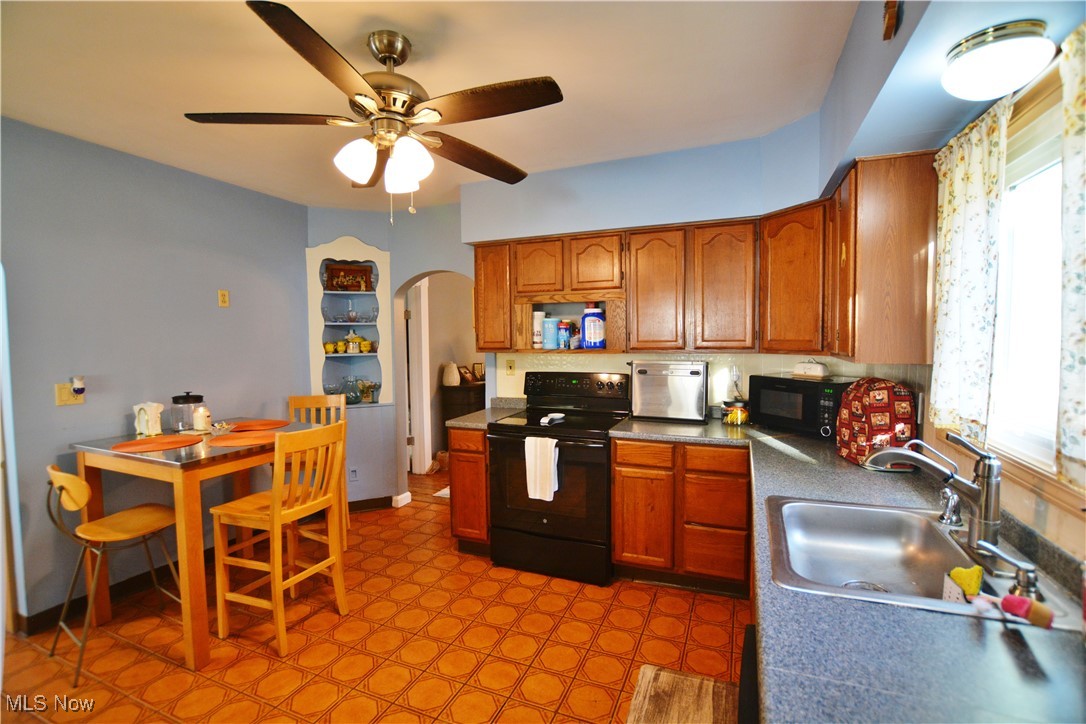 6696 Madison Road Thompson, OH 44086 - Photo 5 of 24 Kitchen with black appliances, brown cabinetry, arched walkways, and ceiling fan