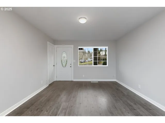 a view of an empty room with window and wooden floor