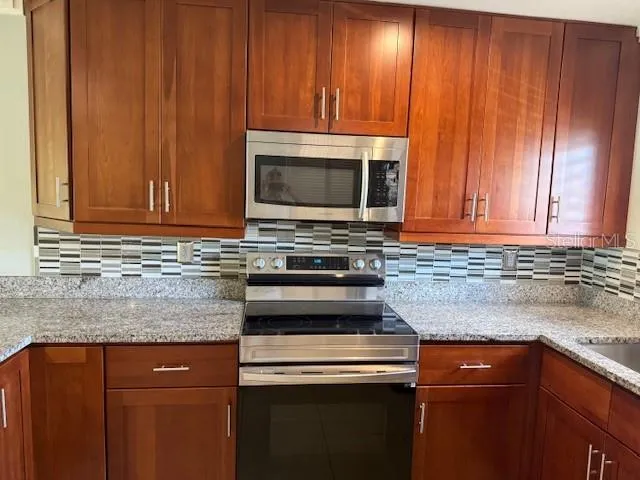 a kitchen with granite countertop wood cabinets stainless steel appliances and a sink