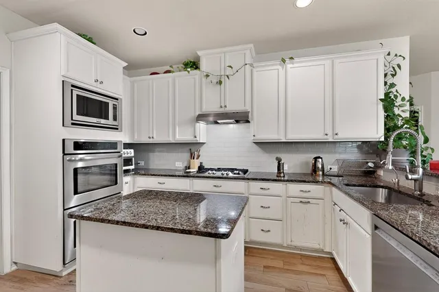 a kitchen with granite countertop a sink stainless steel appliances and white cabinets