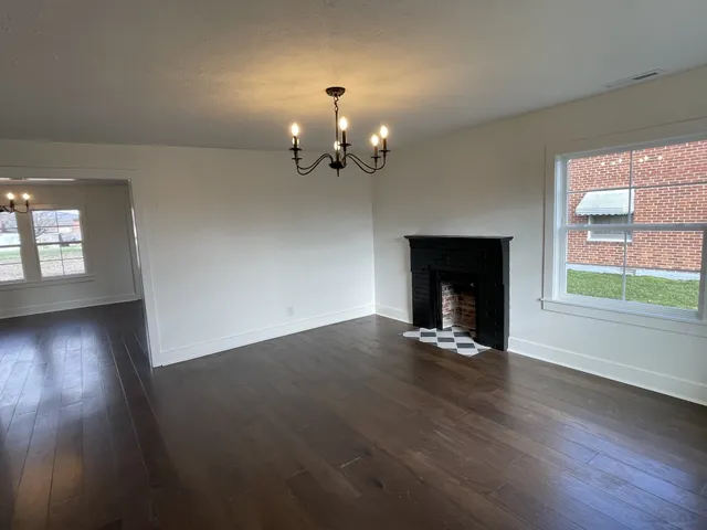 an empty room with wooden floor chandelier and windows