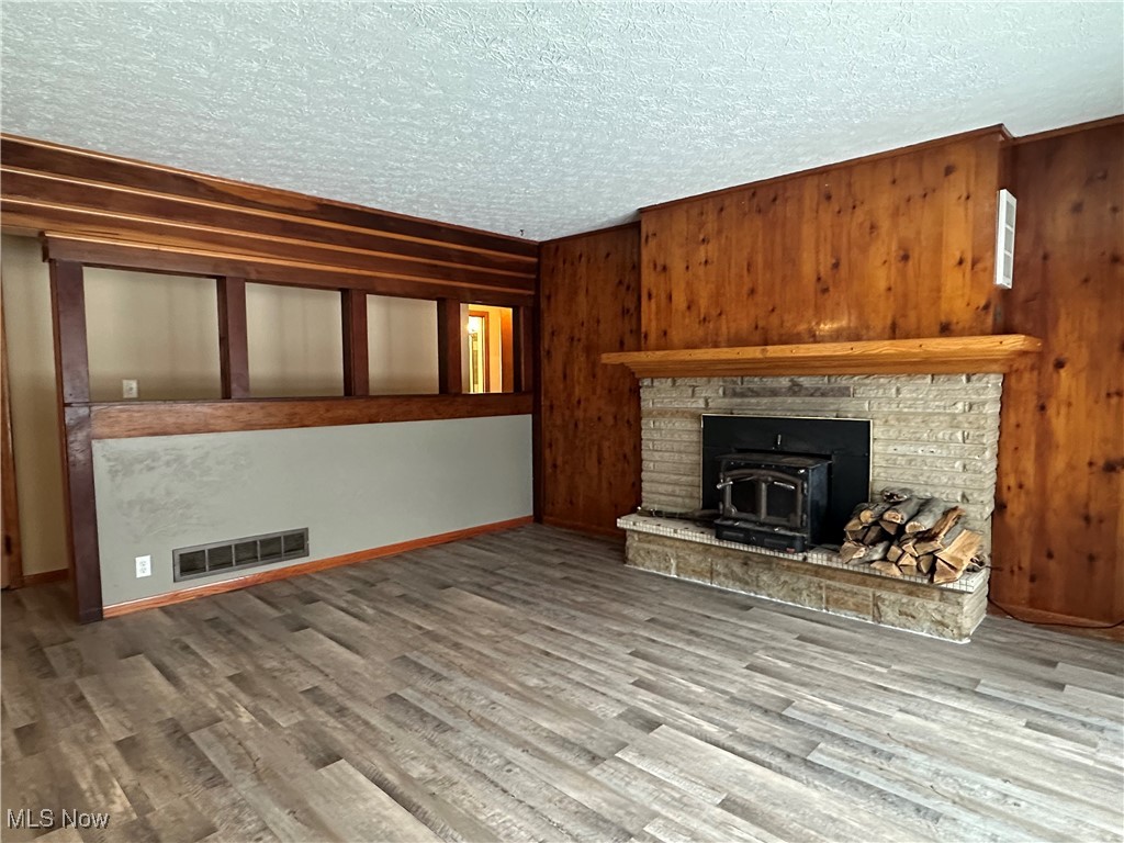 4811 West Pleasant Valley Road Cleveland, OH 44129 - Photo 10 of 31 Unfurnished living room with a wood stove, wood walls, light wood-style floors, and a textured ceiling