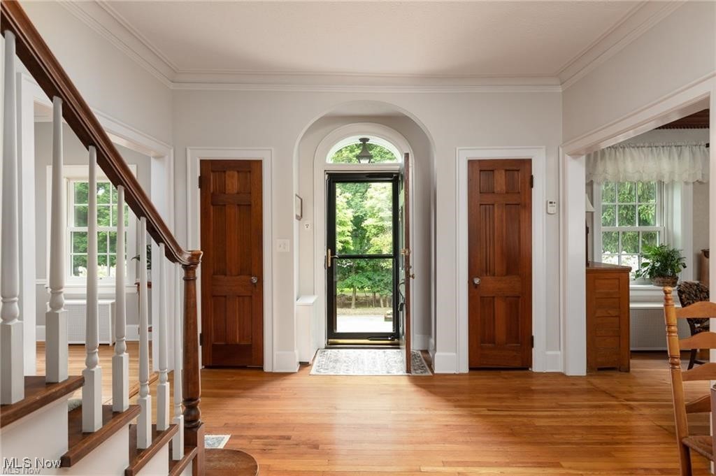 Foyer entrance with light wood finished floors, plenty of natural light, stairs, and crown molding