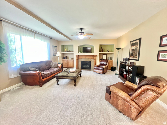 369 Culross Circle Tooele, UT 84074 - Photo 15 of 54 Living area featuring a fireplace with a wood mantle and stone surround, built-in shelving, recessed wall niches, a ceiling fan, and carpet flooring