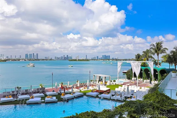 a view of a lake with lawn chairs and large trees