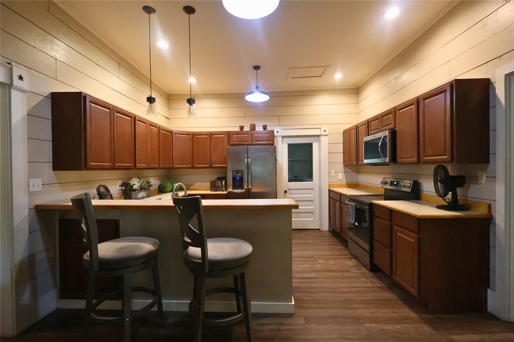 210 Hopkins Street Alba, TX 75410 - Photo 6 of 36 Kitchen with wood walls, appliances with stainless steel finishes, a peninsula, light countertops, and dark wood-type flooring