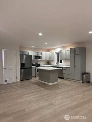 a large white kitchen with kitchen island a sink a stove a oven with white cabinets and wooden floor