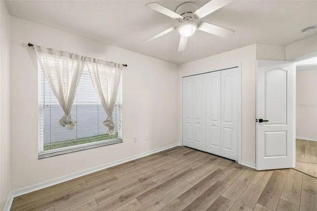 an empty room with wooden floor fan and windows