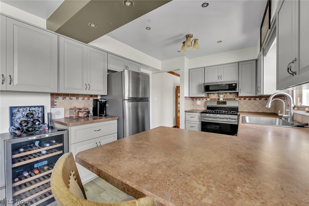 4685 New Road Youngstown, OH 44515 - Photo 16 of 37 Kitchen featuring appliances with stainless steel finishes, tasteful backsplash, gray cabinetry, sink, and wine cooler