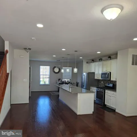 a kitchen with stainless steel appliances kitchen island granite countertop a stove a refrigerator a sink a stove and white cabinets with wooden floor