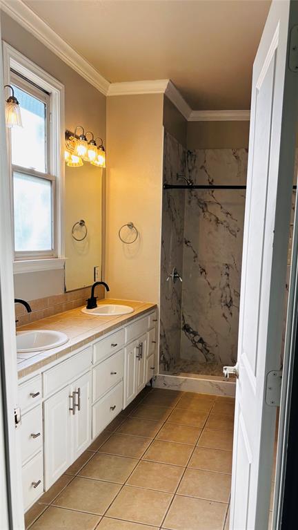 4511 Junius Street Dallas, TX 75246 - Photo 13 of 16 Bathroom featuring a double vanity with white cabinetry and dark bronze hardware, a walk-in shower with marble-look tile, 2 shower heads,and tiled flooring