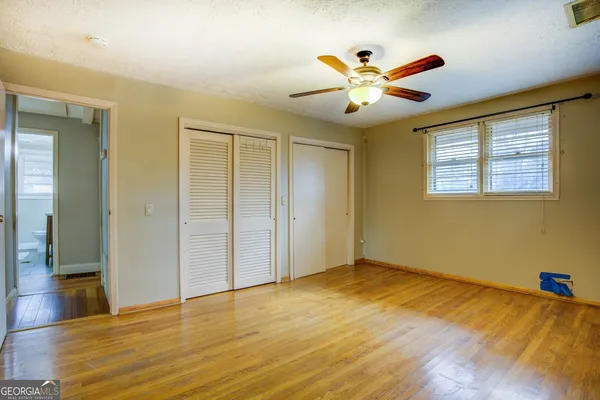 a view of an empty room with wooden floor and a ceiling fan