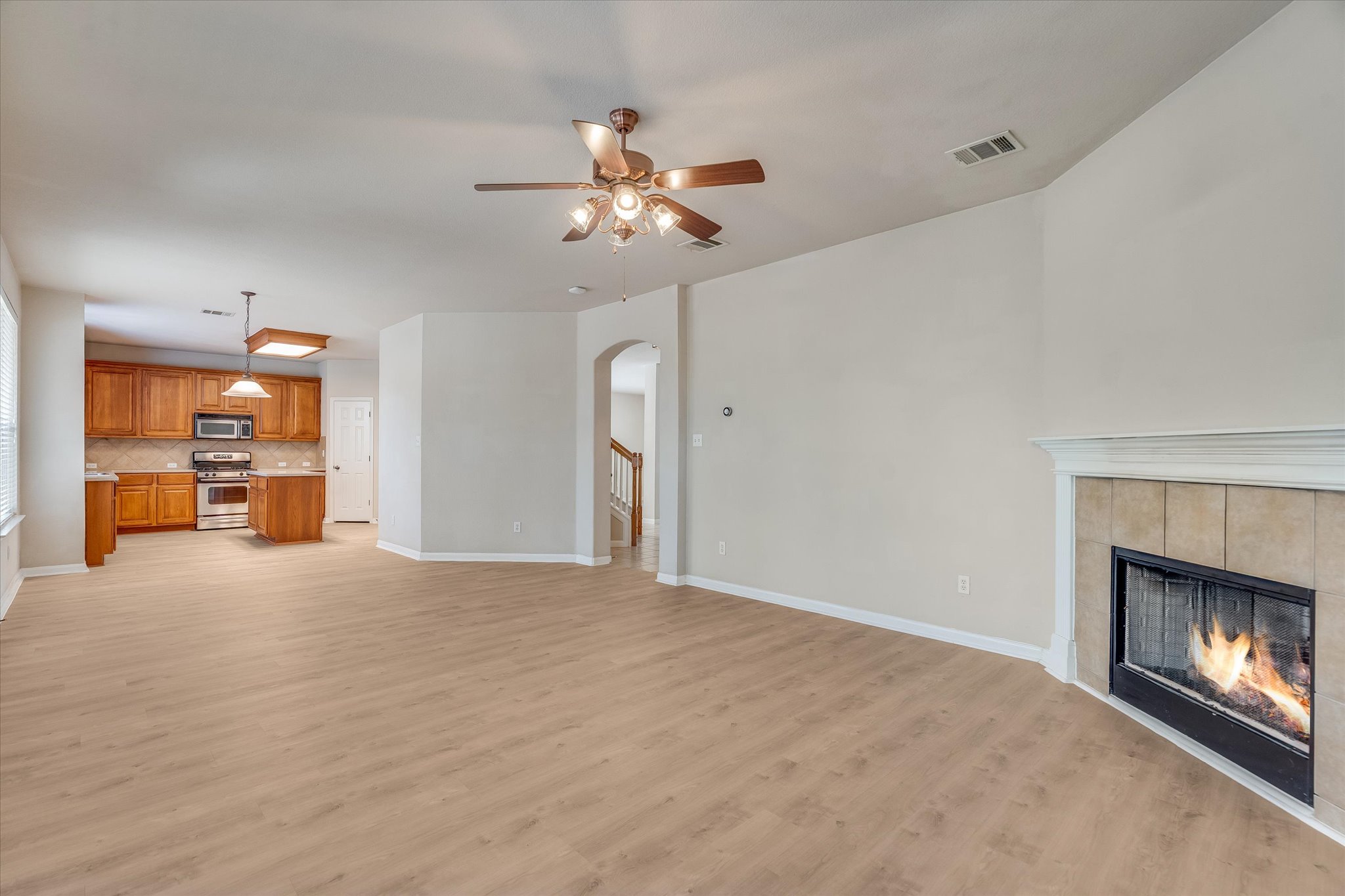 4029 Lake Edge Way Pflugerville, TX 78660 - Photo 8 of 35 Unfurnished living room with a ceiling fan, a tile fireplace, light wood-style flooring, and arched walkways