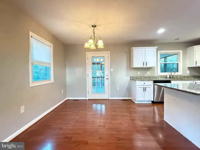 a open kitchen with granite countertop a stove top oven a sink dishwasher and white cabinets with wooden floor