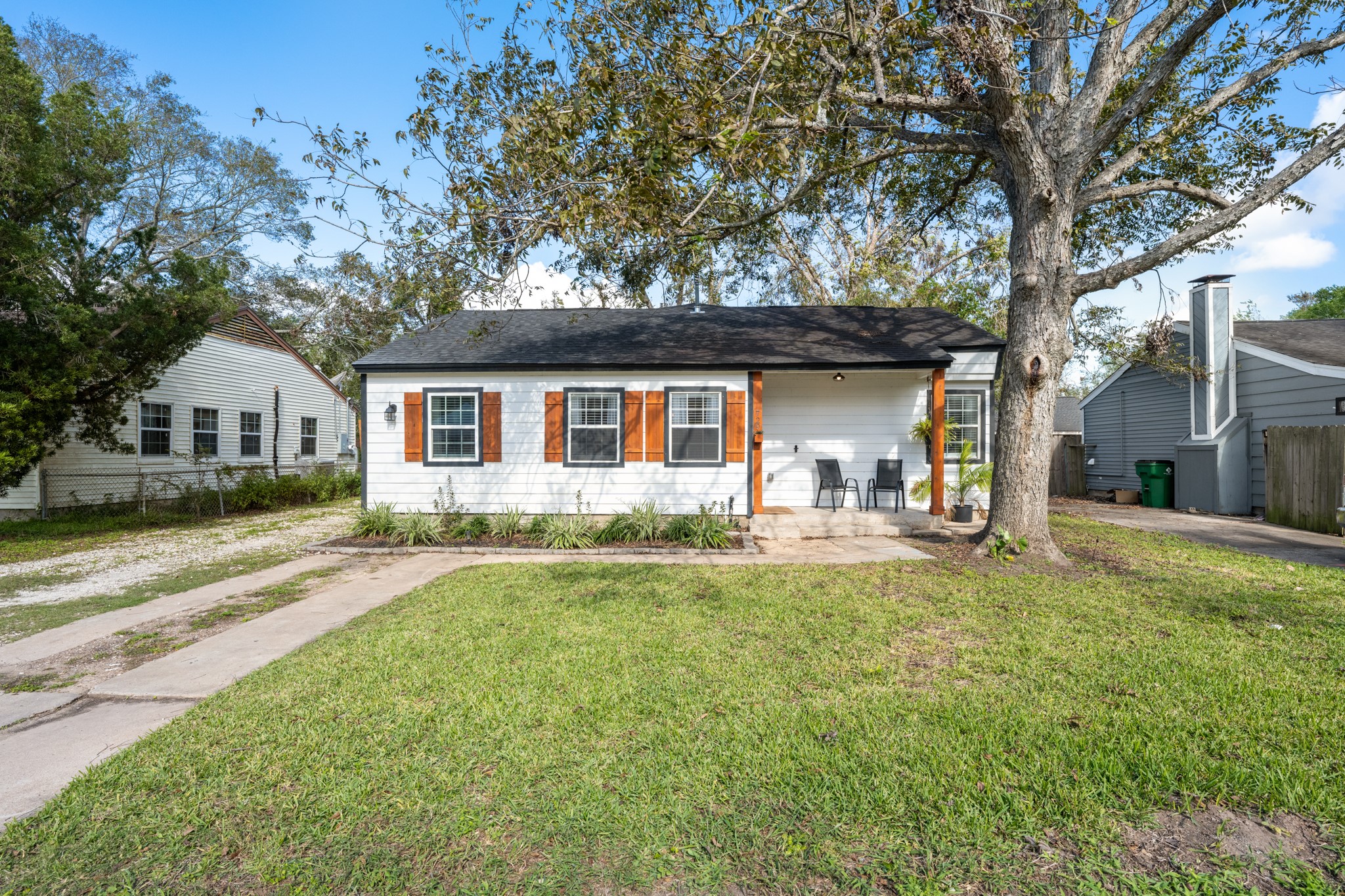 729 Kyle Angleton, TX 77515 - Photo 32 of 36 Charming single-story home with a cozy front porch, nestled under a large tree. It features a neat lawn and a driveway, offering a welcoming and serene atmosphere.