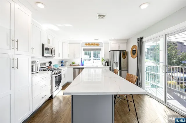 a large white kitchen with granite countertop a stove a sink a refrigerator and white cabinets with wooden floor