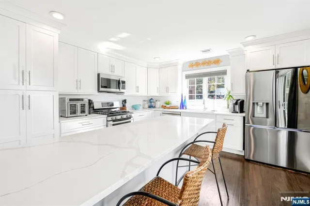 a kitchen with stainless steel appliances granite countertop a refrigerator a stove a sink a dining table and chairs with wooden floor