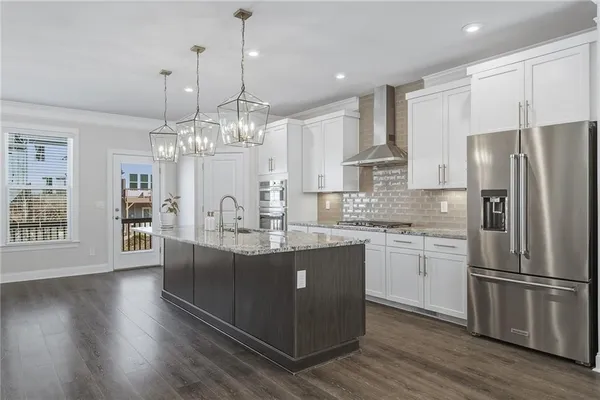 a kitchen with stainless steel appliances granite countertop a refrigerator a sink dishwasher a oven and a dining table with wooden floor