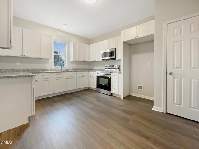 a kitchen with stainless steel appliances granite countertop a stove top oven a sink and white cabinets with wooden floor