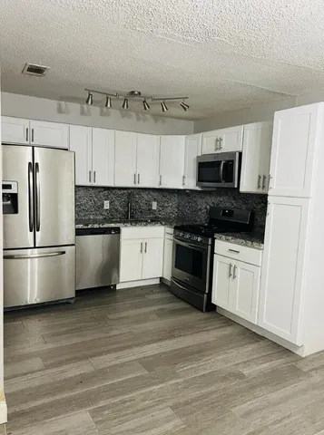 a kitchen with granite countertop a refrigerator stove and white cabinets