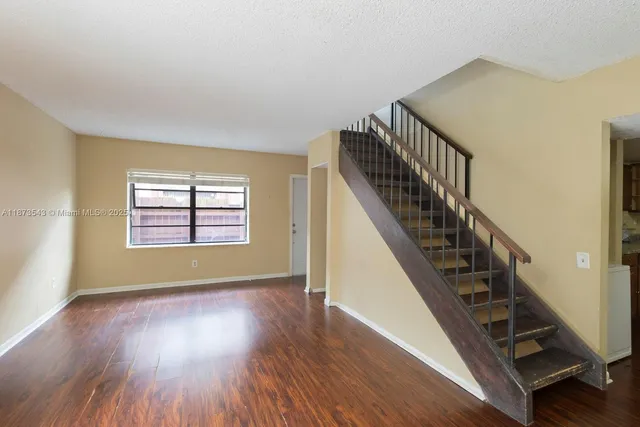 a view of an empty room with wooden floor and fan