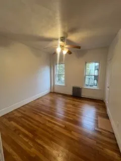 an empty room with wooden floor chandelier fan and windows
