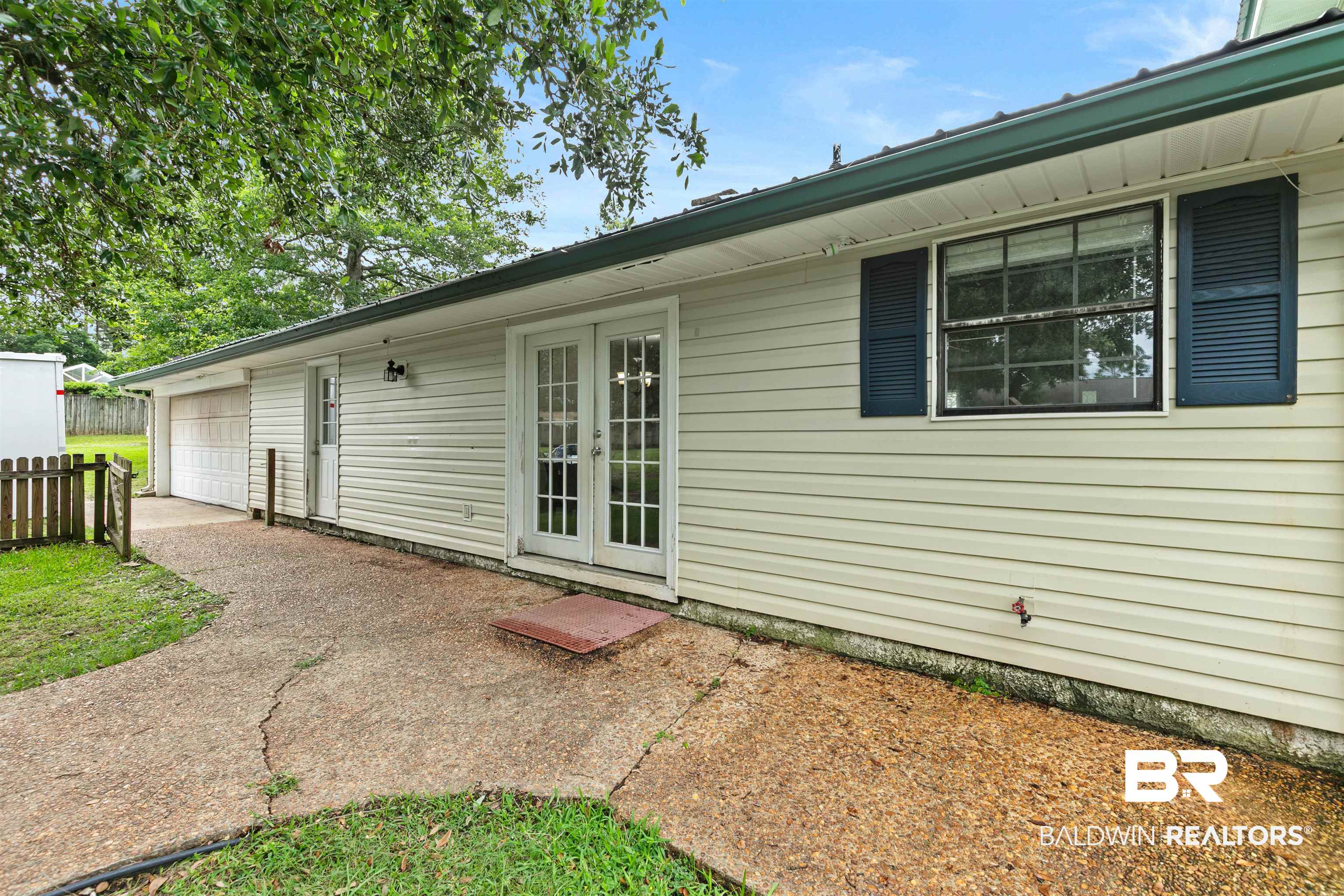 10420 Johnson Road South Mobile, AL 36695 - Photo 63 of 75 White siding exterior featuring double glass-paneled doors, a single window with dark louvered shutters, and a dark green metal roof