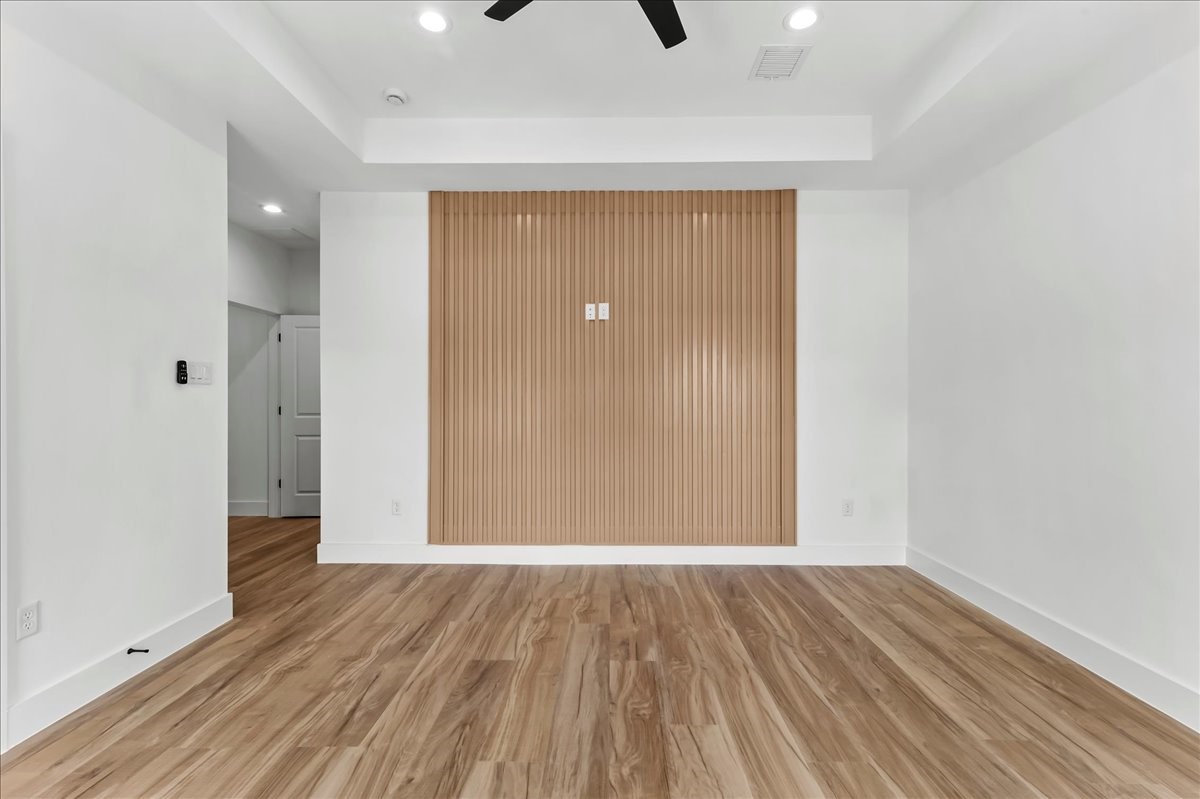 8323 Observatory Street, Unit A/B Houston, TX 77088 - Photo 24 of 38 Unit B - Spacious primary suite featuring a beautiful neutral-toned accent wall that perfectly complements the wood-look flooring, elegant coffered ceiling, and a remote-controlled ceiling fan. Accent Wall design may vary. Pictures are from a previous build.