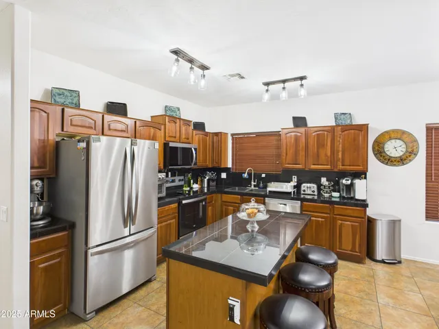 a kitchen with stainless steel appliances granite countertop a refrigerator a stove top oven a chimney and a center island