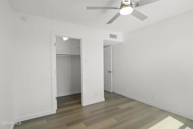 an empty room with wooden floor fan and windows