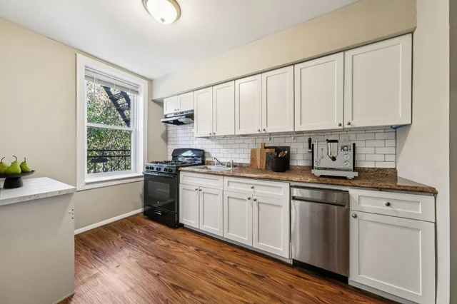 a kitchen with stainless steel appliances granite countertop a stove a sink and white cabinets with wooden floor